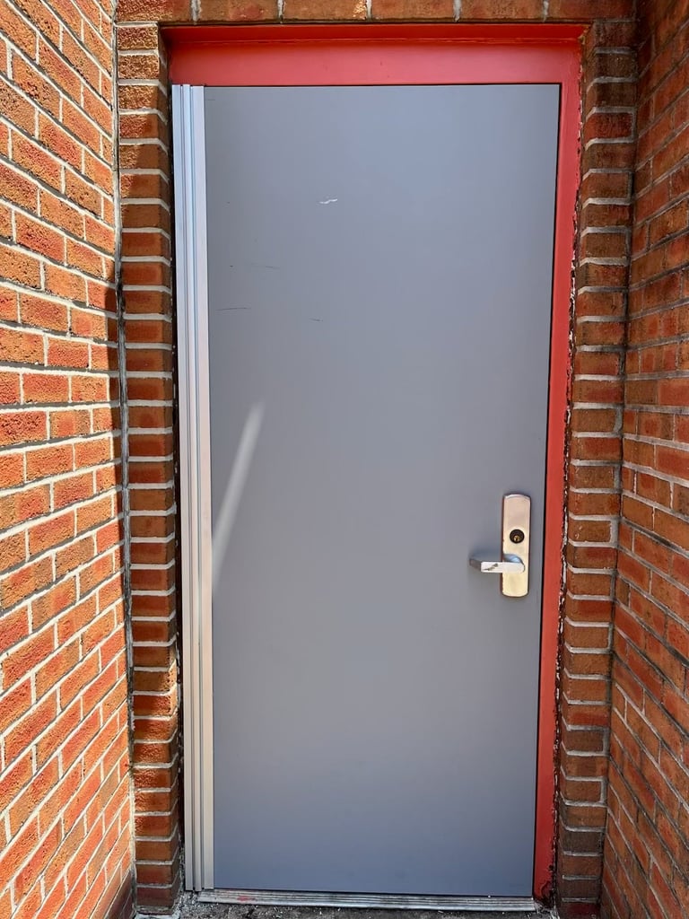Gray door with silver handle set in a red frame between two red brick walls
