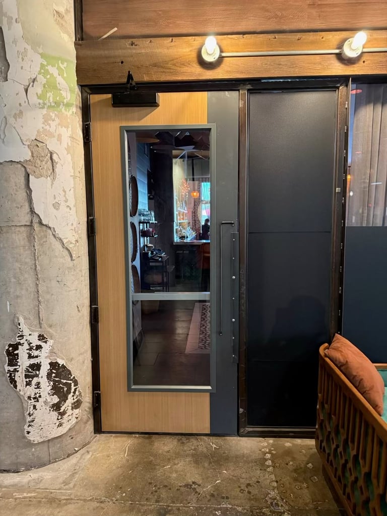 Glass and black metal sliding doors entrance to a dimly lit establishment with wooden trim and wall sconces above