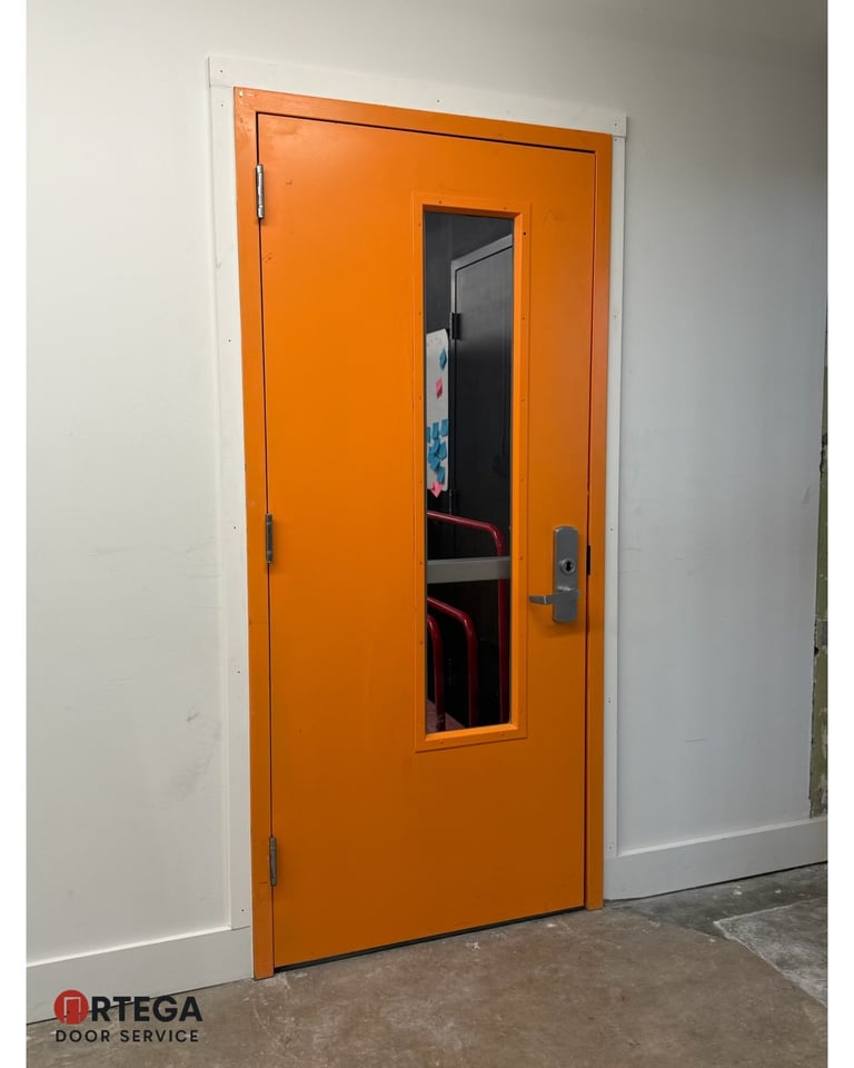 Bright orange industrial door with small rectangular window and metal handle in white-walled room