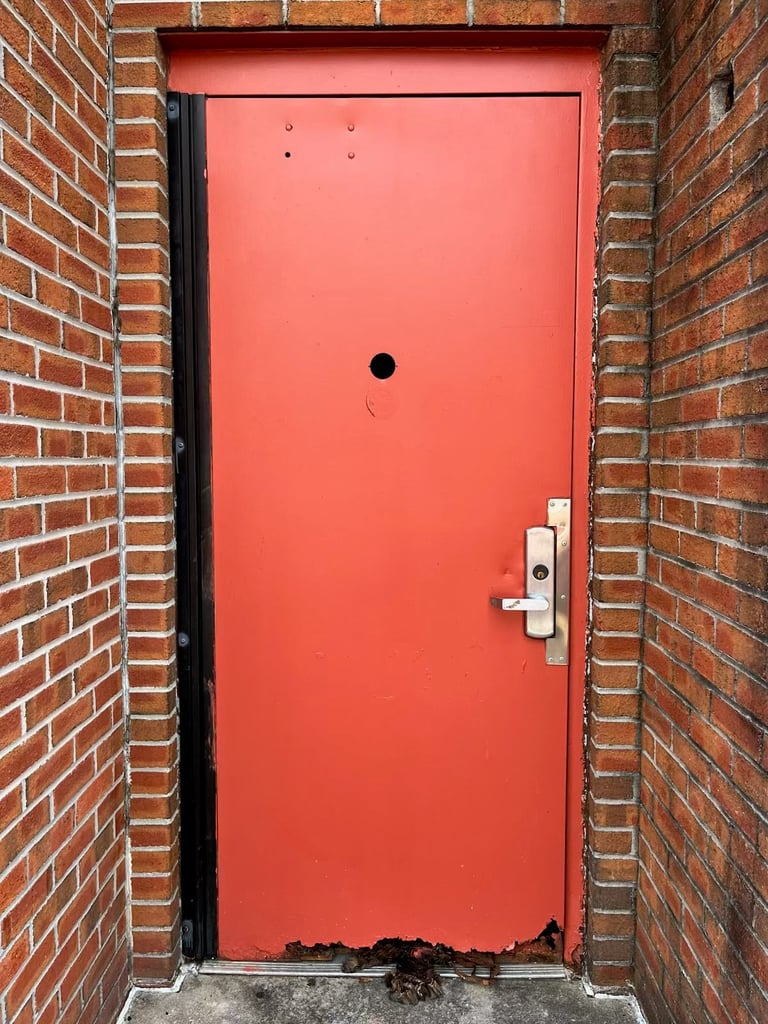 Bright red metal door set in a brick wall with a silver handle and peephole